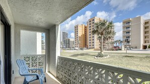 Ein Balkon mit blauem Stuhl, weißem Ziergeländer und Blick auf hohe Gebäude und Palmen.