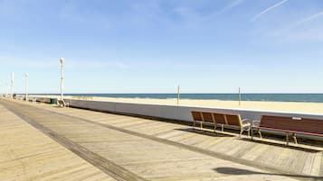 A wooden boardwalk leading to a beach with benches and street lamps.