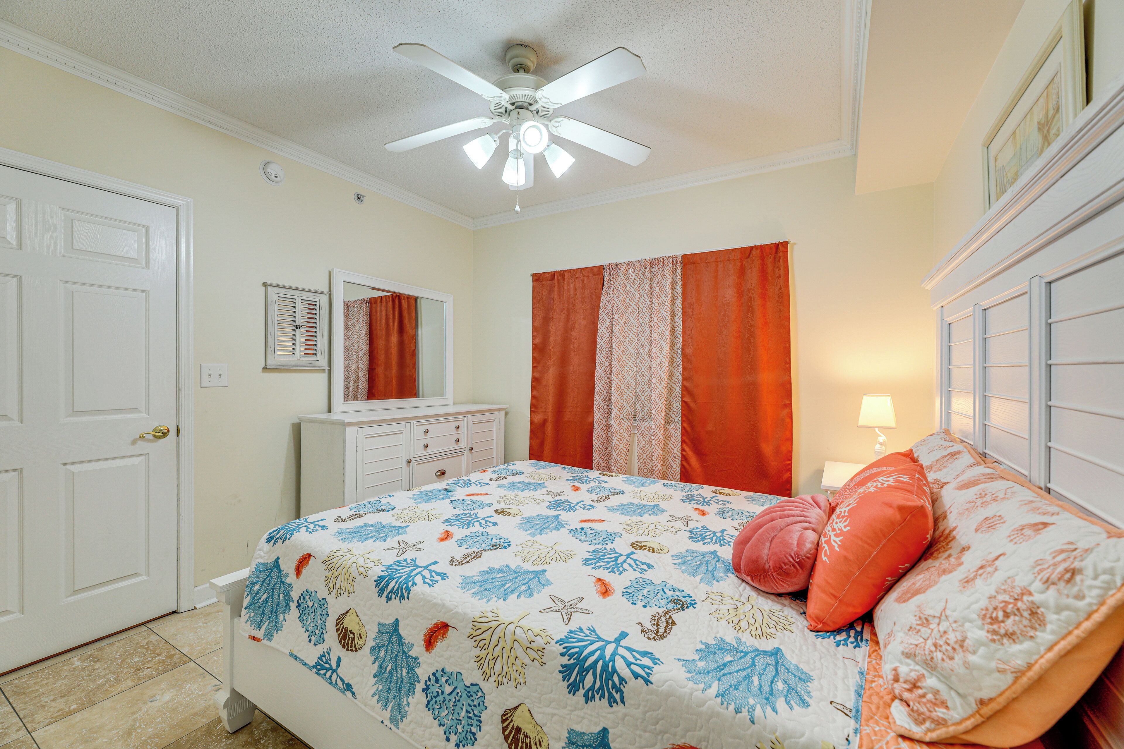 A bedroom with a bed, a ceiling fan, a dresser, a mirror, and a window with curtains.
