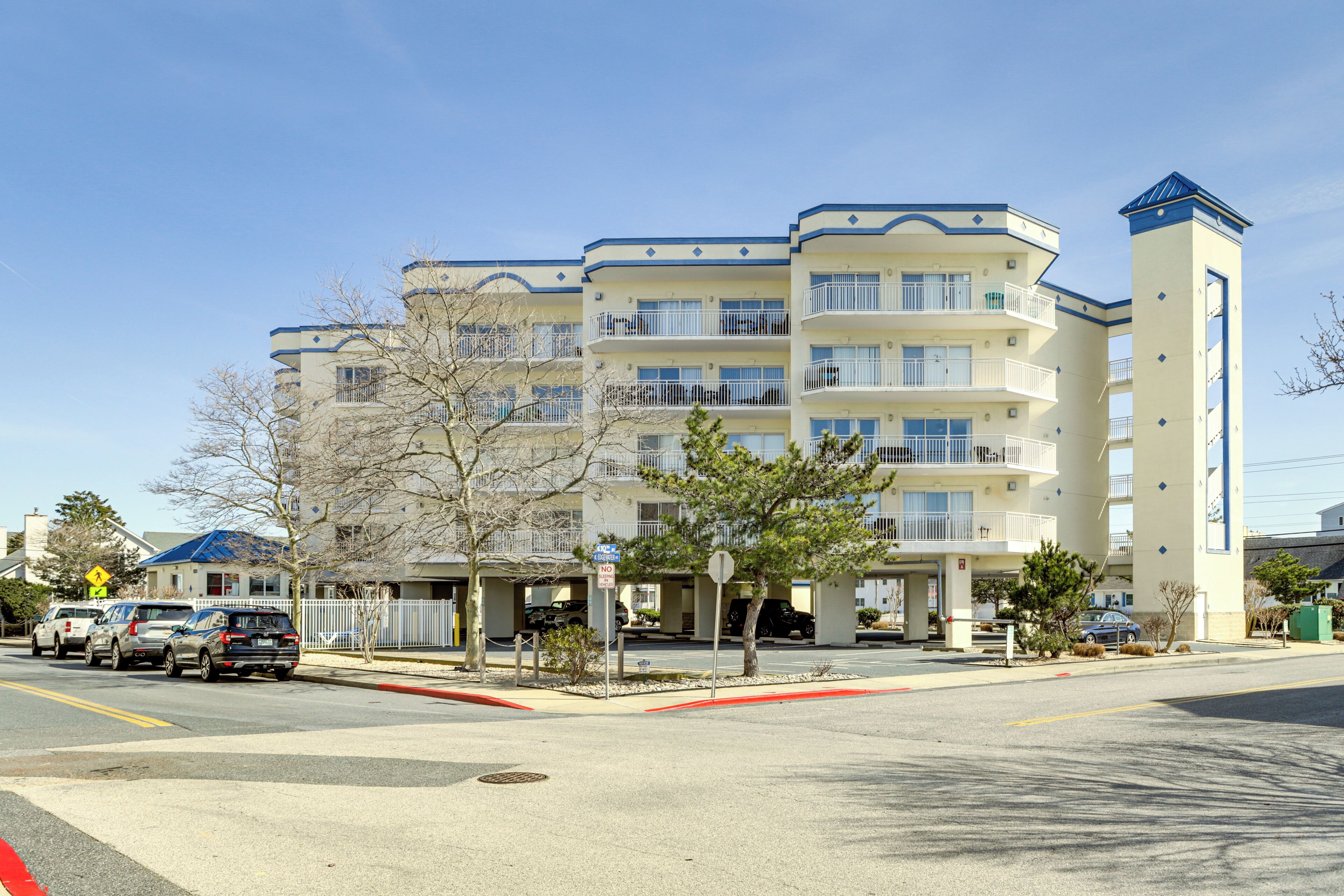 A multi-story hotel with balconies, a parking area, and a clear sky.