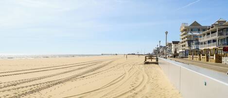 A beach with a boardwalk, buildings, and a pier in the background.