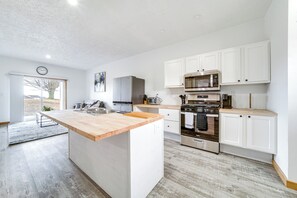 Een moderne keuken met witte kastjes, een houten eiland, roestvrijstalen apparatuur en een groot raam.