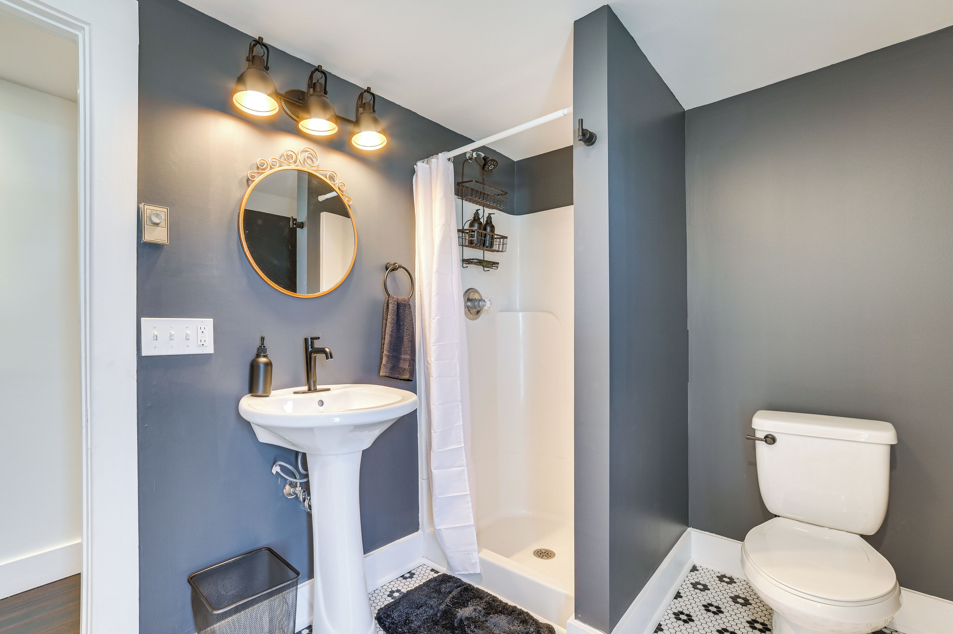 A bathroom with a pedestal sink, a round mirror, a shower with a white curtain, and a toilet.