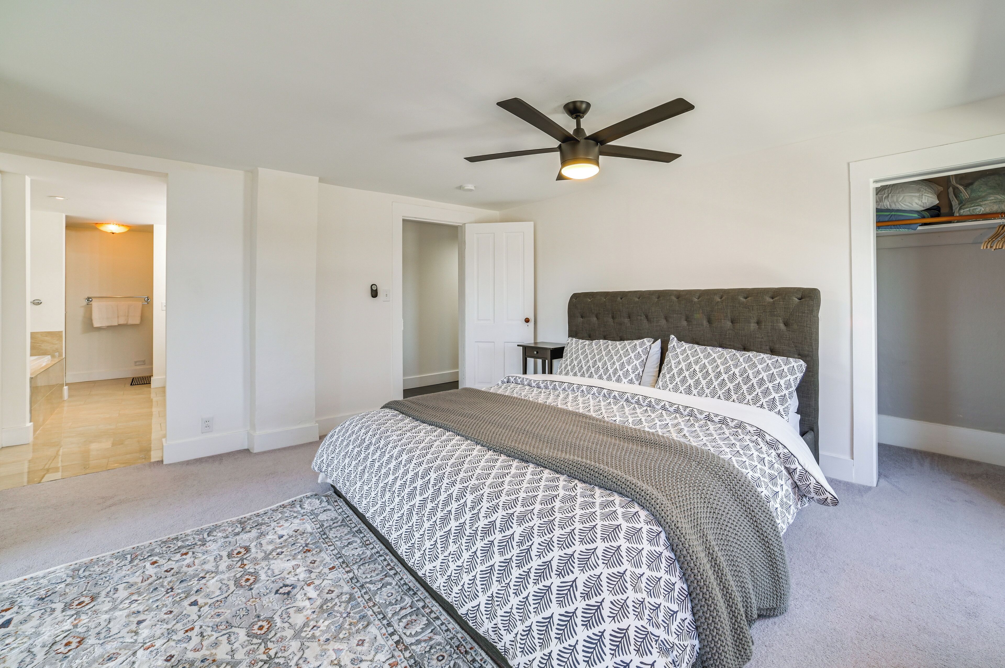 Une chambre avec un grand lit, un ventilateur de plafond et un dressing.