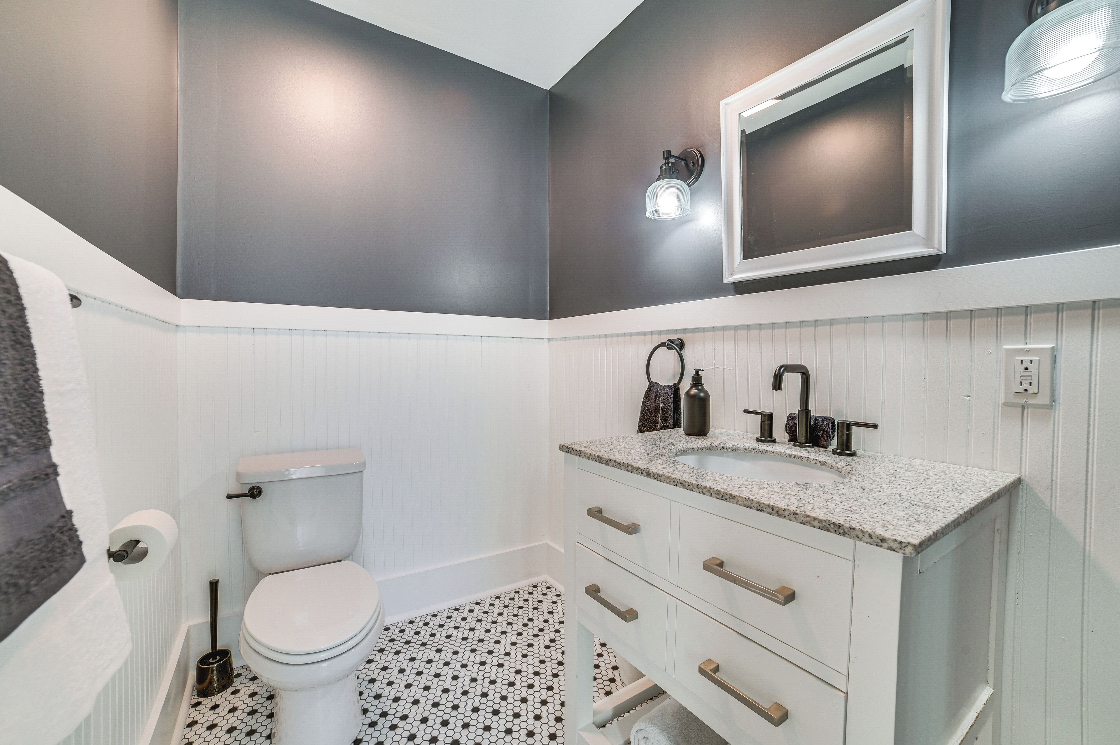 Een badkamer met een toilet, een witte wastafel met een granieten aanrechtblad en een spiegel aan de muur.