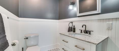 Een badkamer met een toilet, een witte wastafel met een granieten aanrechtblad en een spiegel aan de muur.