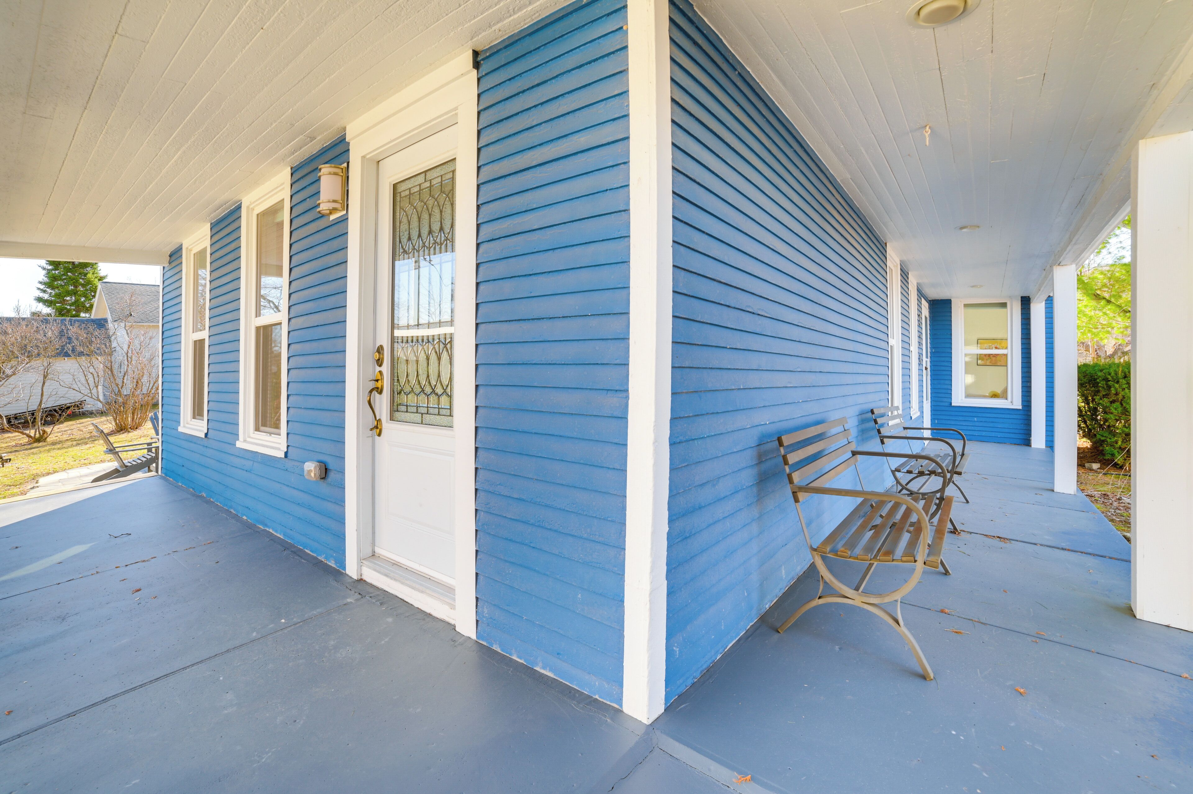 Une maison bleue avec un porche abrité, une porte d’entrée et deux bancs.