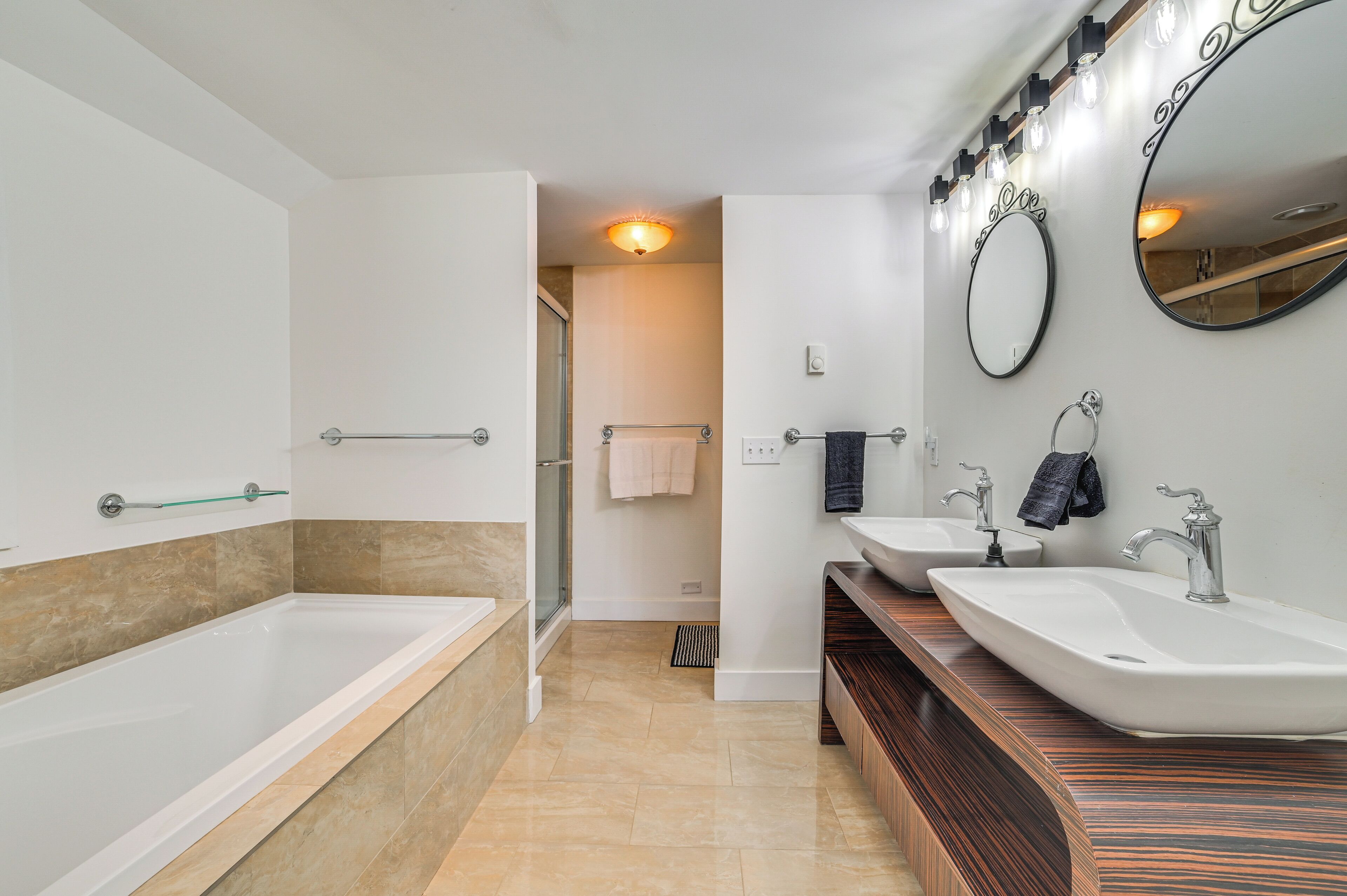 A modern bathroom with a bathtub, two sinks, and a large mirror.