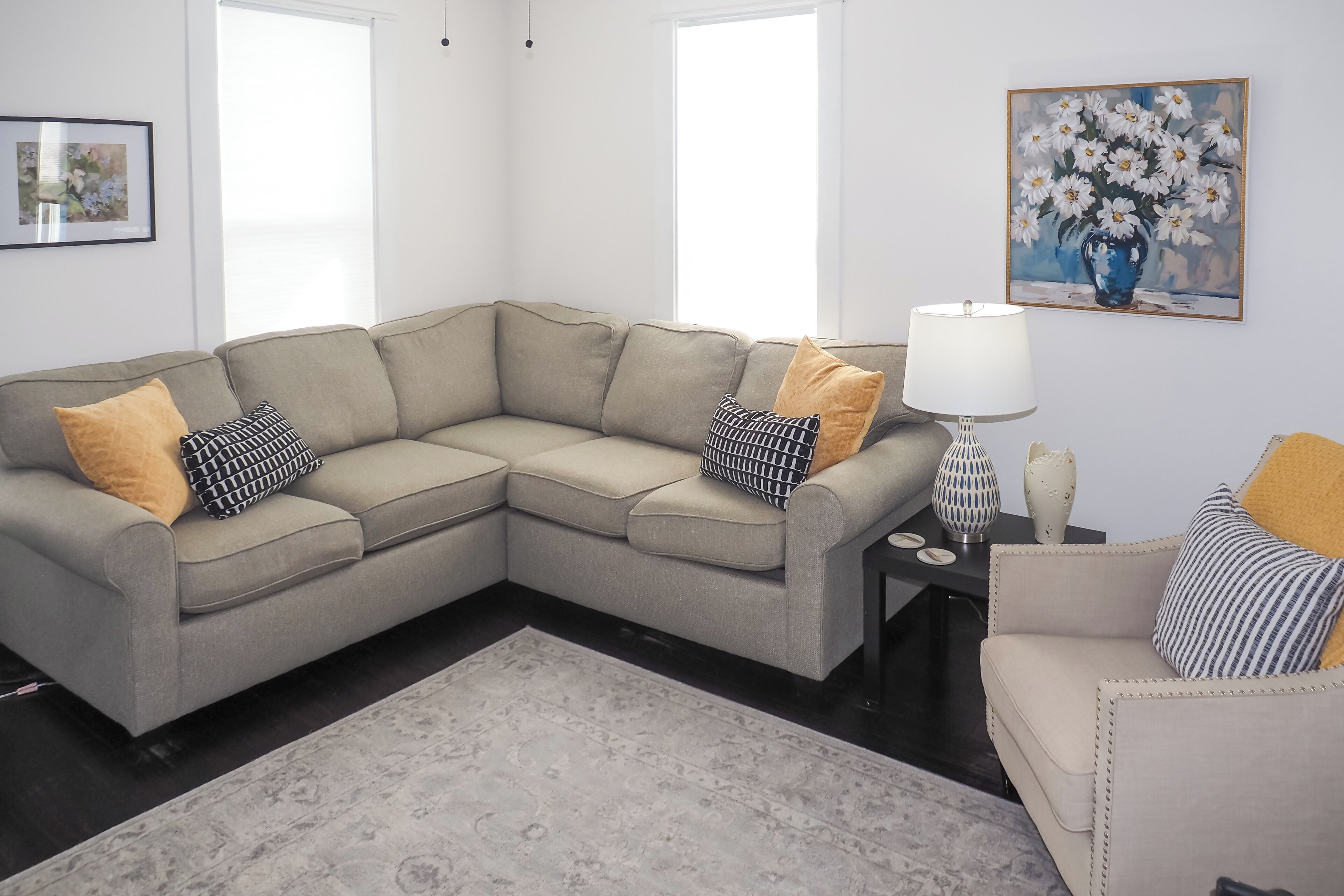 A modern living room with a grey sectional sofa, a small side table, a floor lamp, and a painting of flowers on the wall.