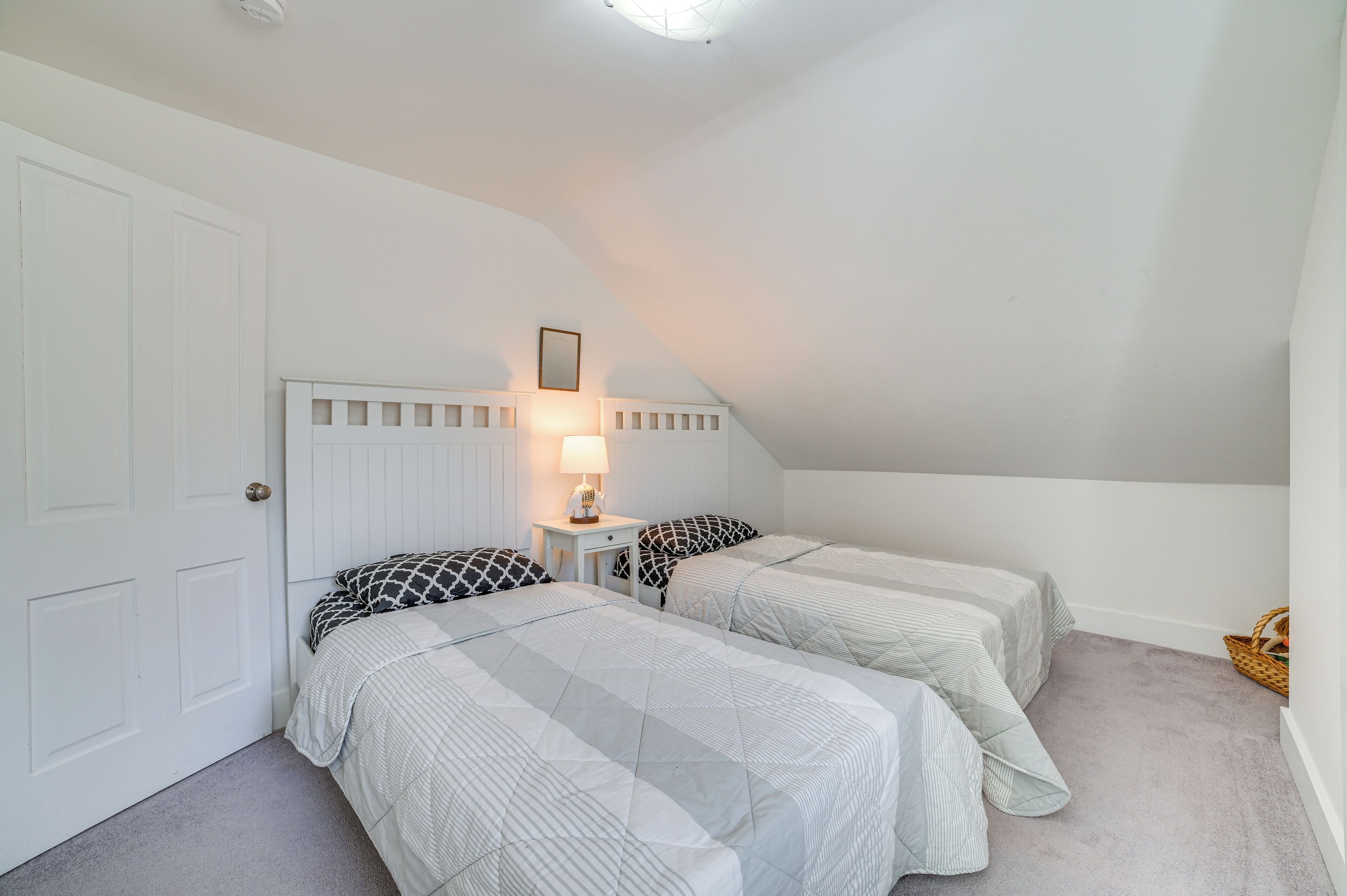 A bedroom with two beds, a nightstand with a lamp, and a white door.