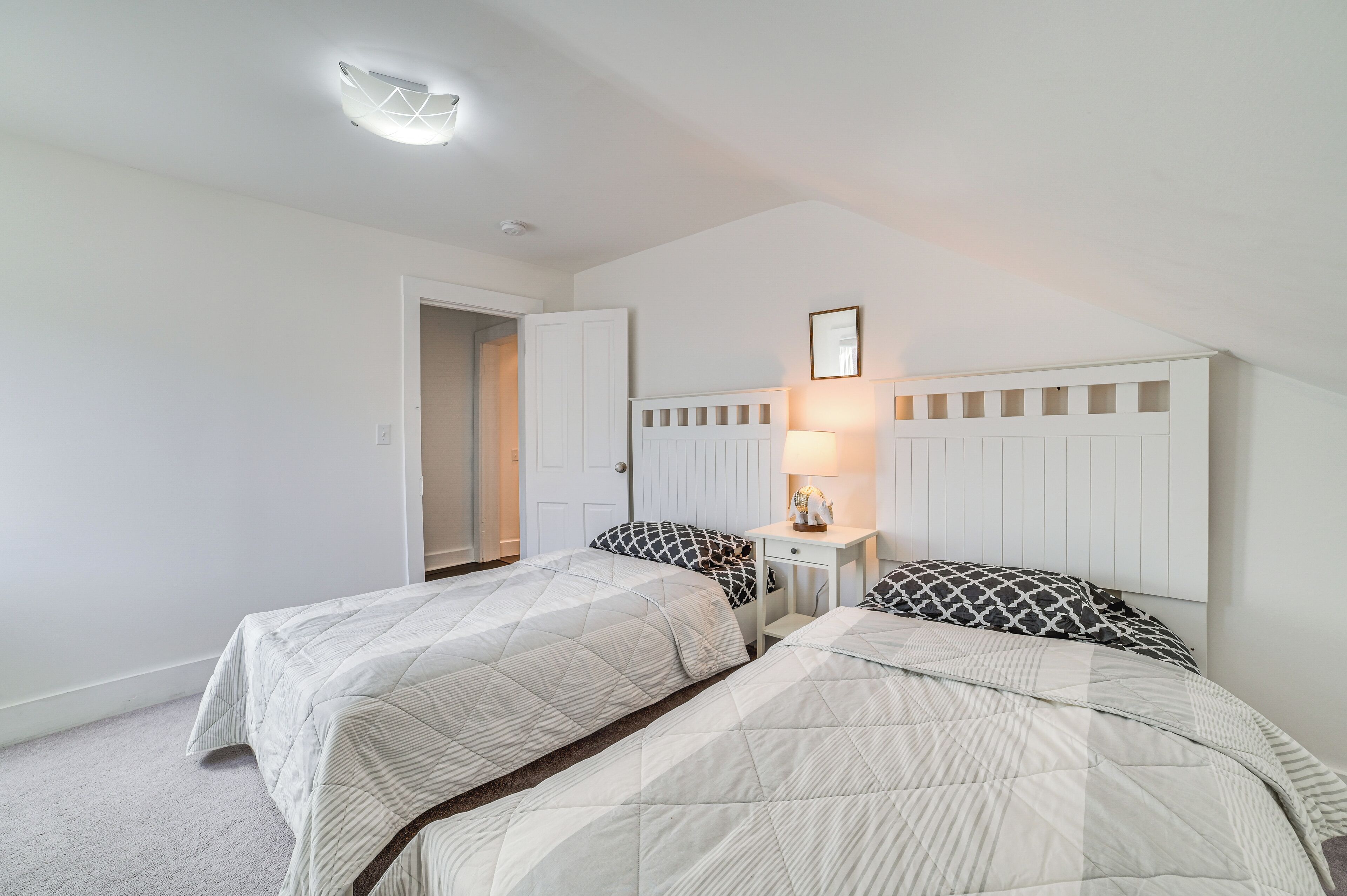 A bedroom with two beds, a nightstand, a lamp, and a door leading to another room.