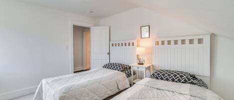 A bedroom with two beds, a nightstand, a lamp, and a door leading to another room.