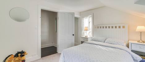 A bedroom with a bed, a nightstand, a lamp, a rocking horse, and a door leading to another room.