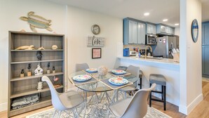 A modern kitchen with blue cabinets, a central island, and a dining area with a glass table and gray chairs.