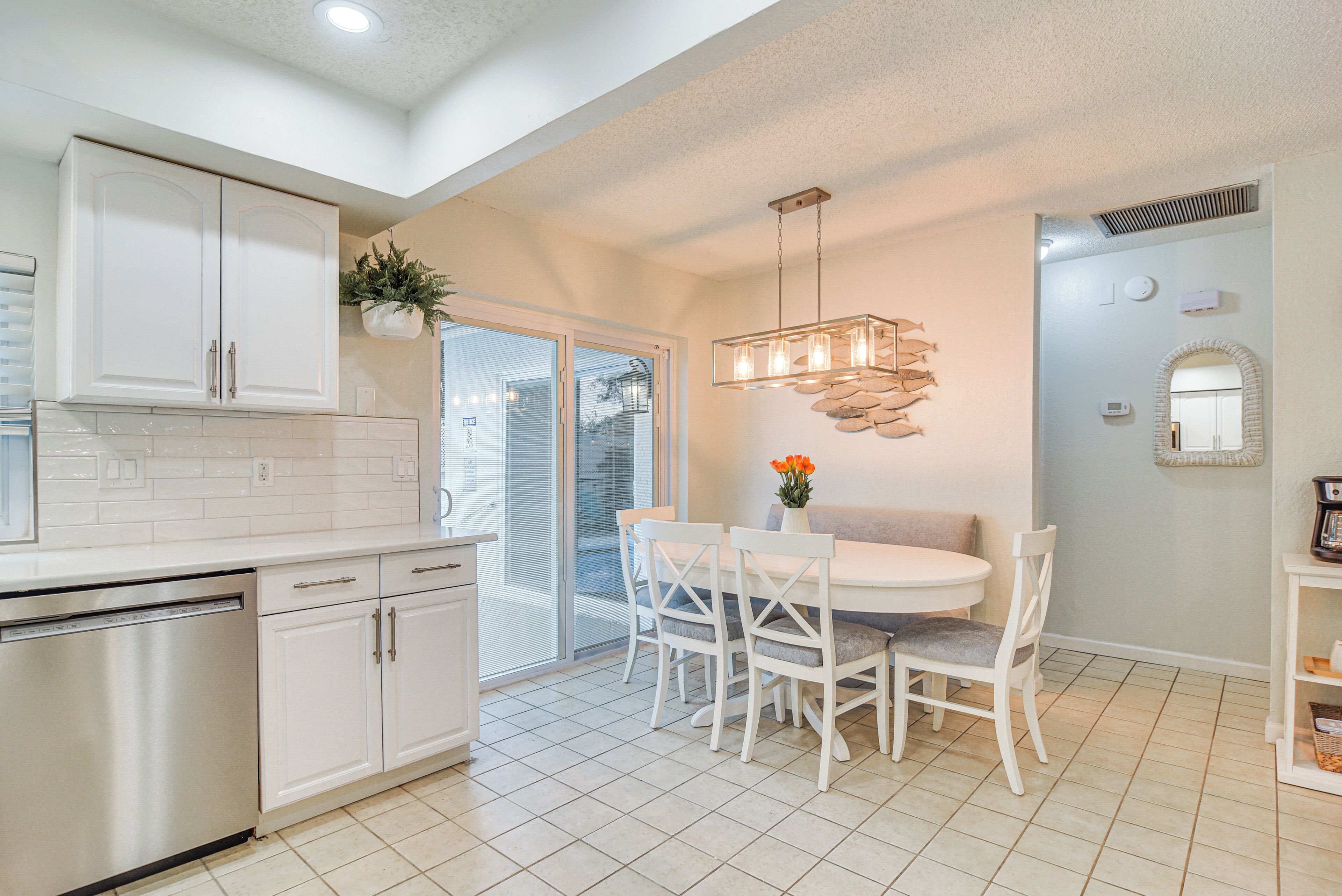 A modern kitchen with white cabinetry, a built-in dishwasher, and a dining area with a round table and white chairs.