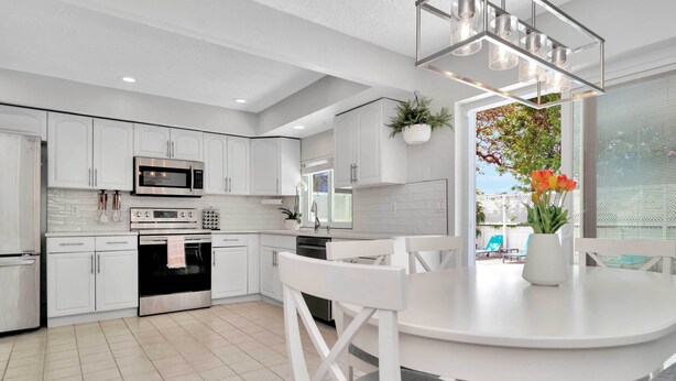 A modern kitchen with white cabinetry, a stainless steel oven, and a dining area with a white table and chairs. - Charming Largo Home w/ Private Pool: 1 Mi to Beach (Largo)