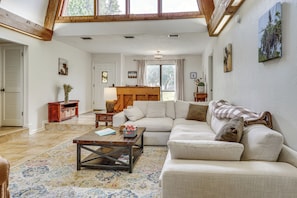 A spacious living room with a high ceiling, a wooden coffee table, a beige sofa, and a large window.