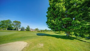 A well-maintained grassy area with a large tree, a clear sky, and distant buildings. - 4 Mi to Lake Erie: Condo w/ Golf Course Views! (Erie)