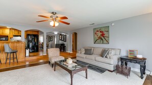 Un salon spacieux comprenant un canapé, un fauteuil, une table basse et un coin repas avec des meubles de rangement en bois et un réfrigérateur.