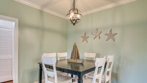 A dining room with a dark wooden table surrounded by white chairs, a chandelier, and three starfish wall decorations. - Foley Condo w/ Pool Access: 10 Mi to Gulf Shores! (Foley)