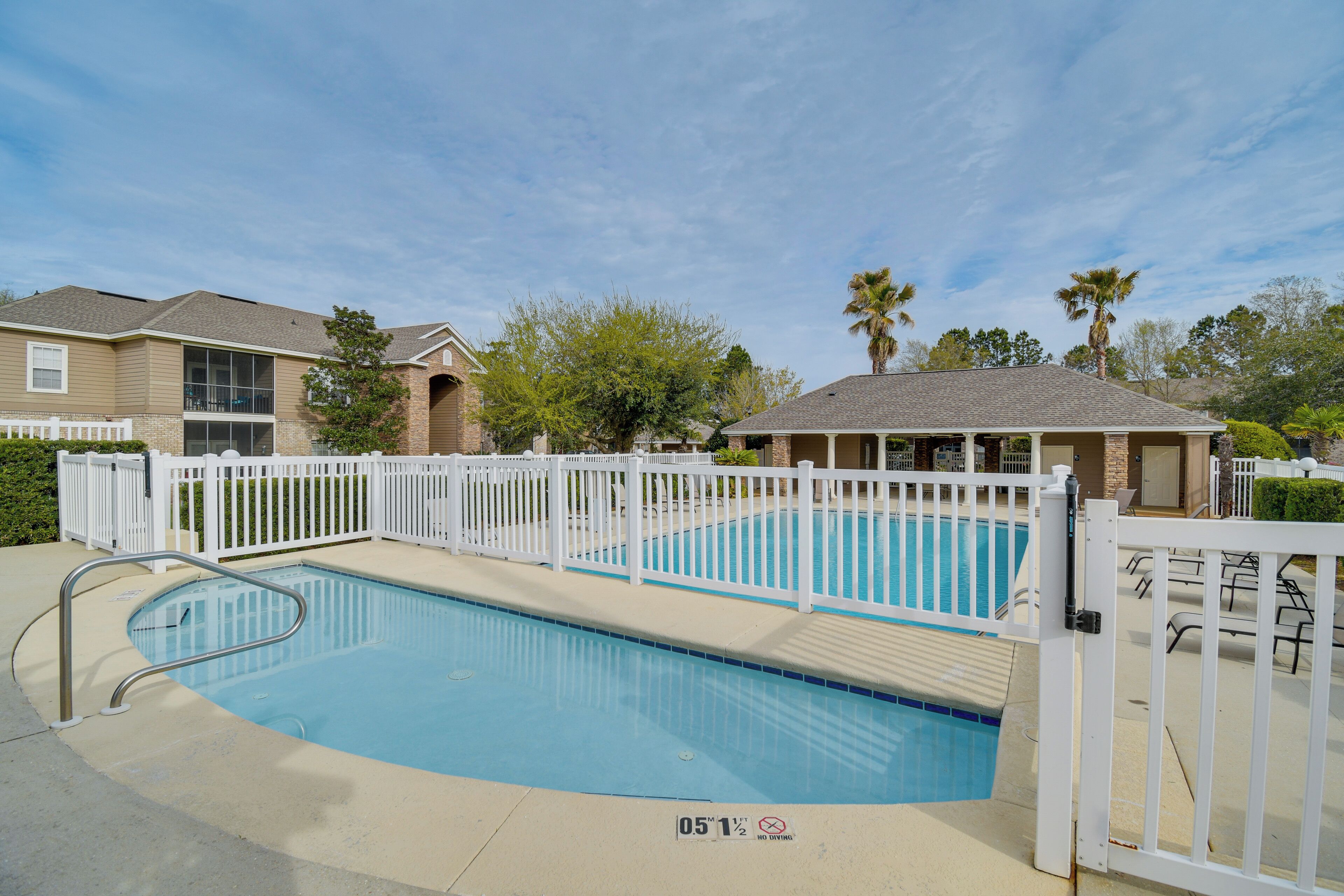 A swimming pool with a white fence, a lifeguard stand, and a covered seating area.