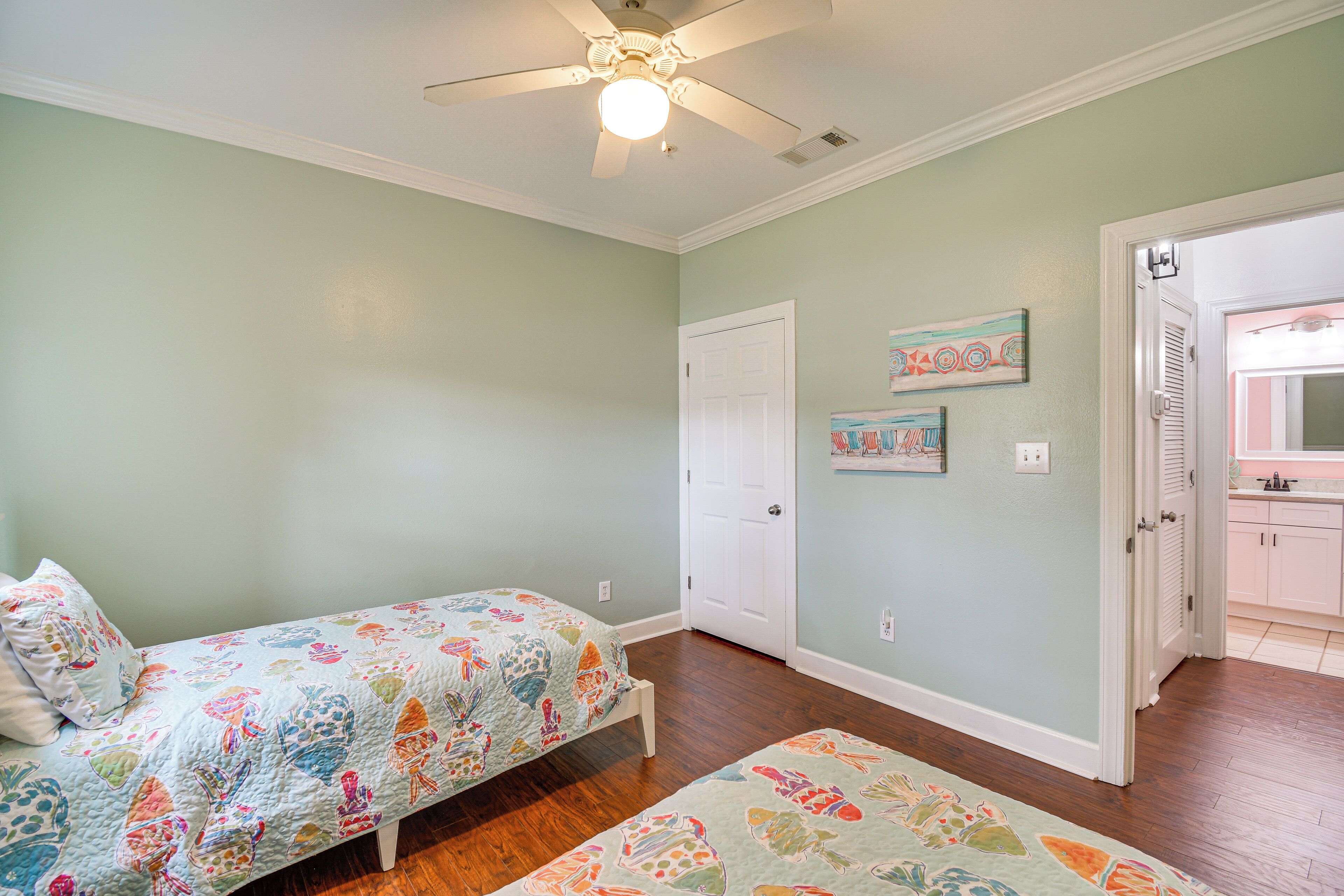 A bedroom with two beds, a ceiling fan, and a door leading to a bathroom.