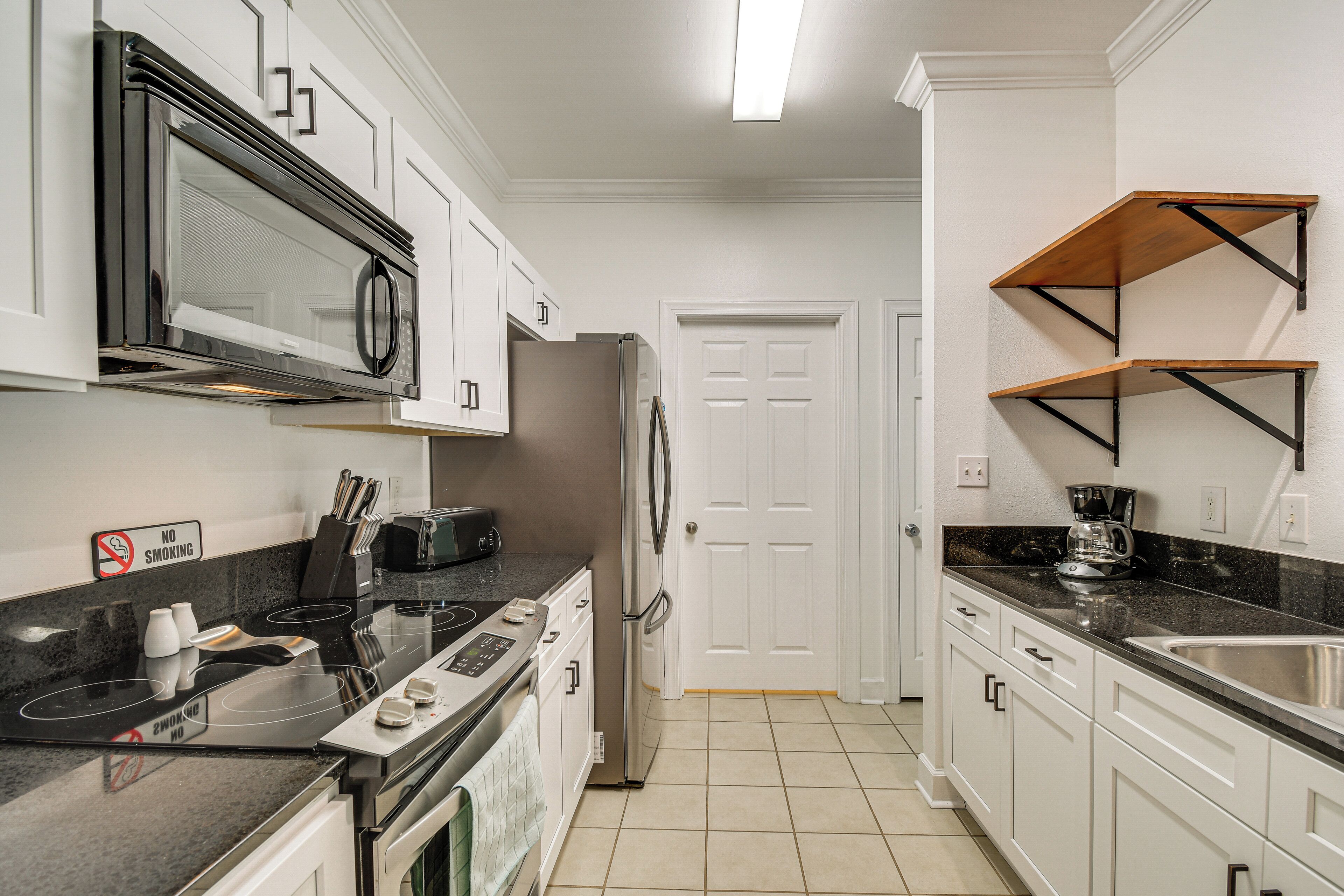 A kitchen with white cabinets, a stainless steel refrigerator, a microwave, and a stove.