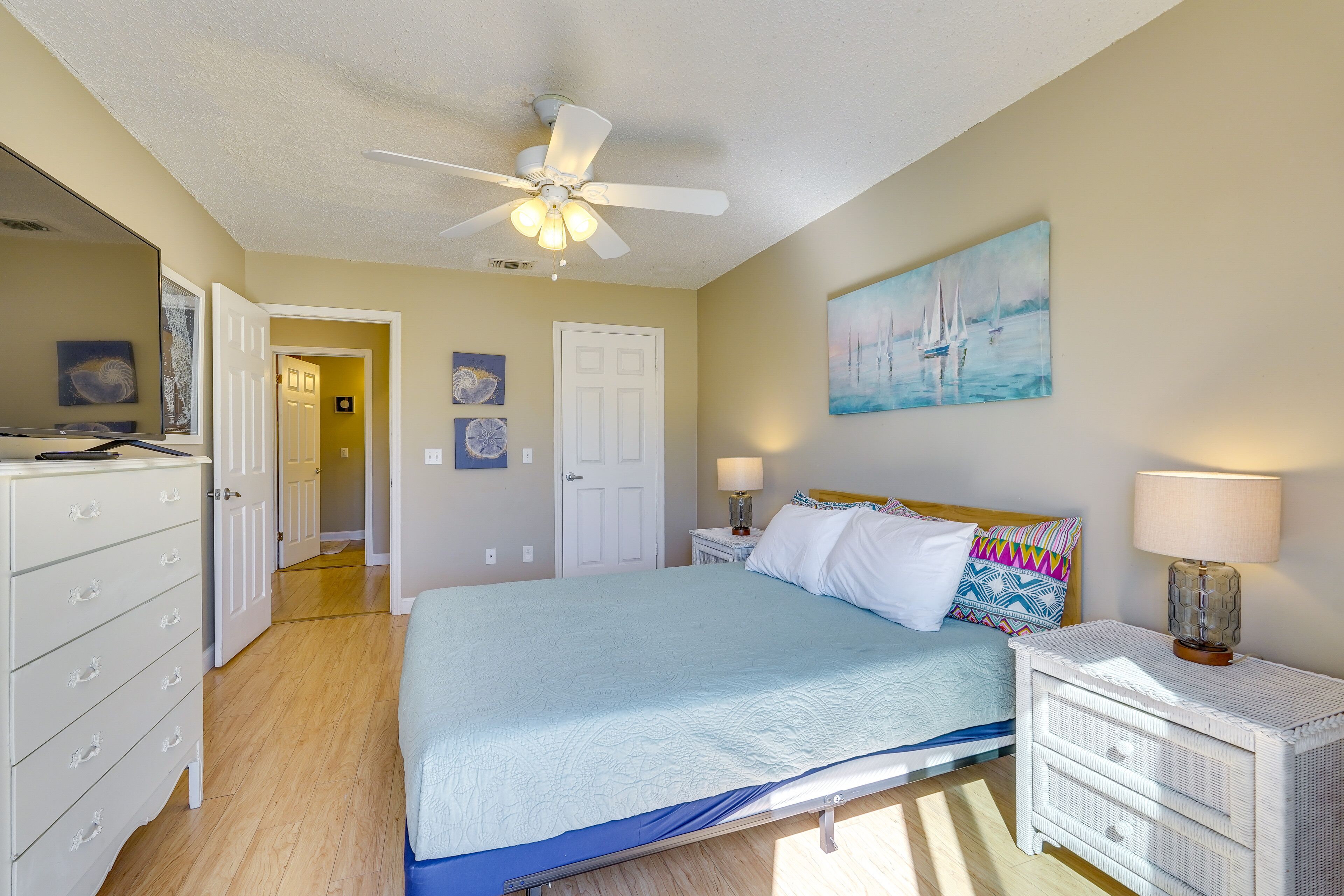 A bedroom with a bed, a nightstand, a dresser, a ceiling fan, and a door.