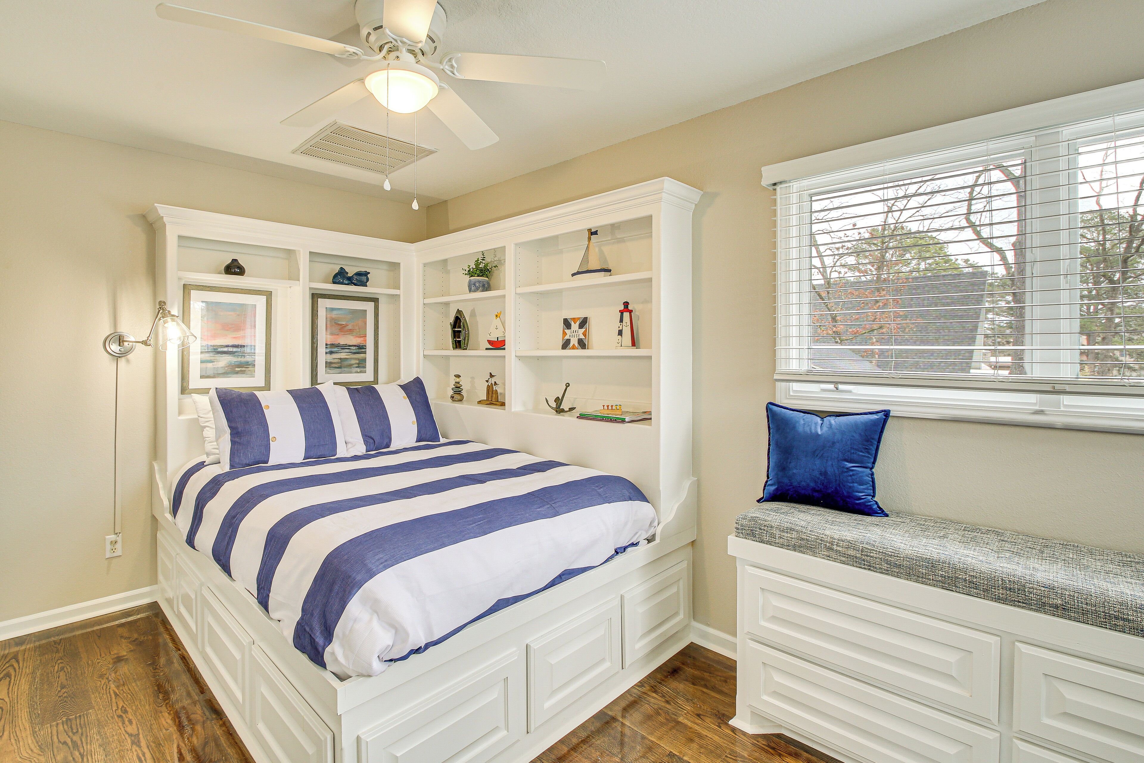 A bedroom with a bed, built-in shelving, a bench, and a ceiling fan.