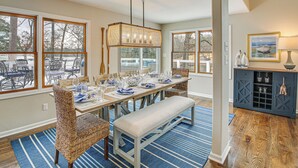 A dining area with a long table set for six, surrounded by wicker chairs, a bench, and a blue striped rug. - Hot Springs Lakefront Home w/ Dock & Water Views! (Hot Springs)