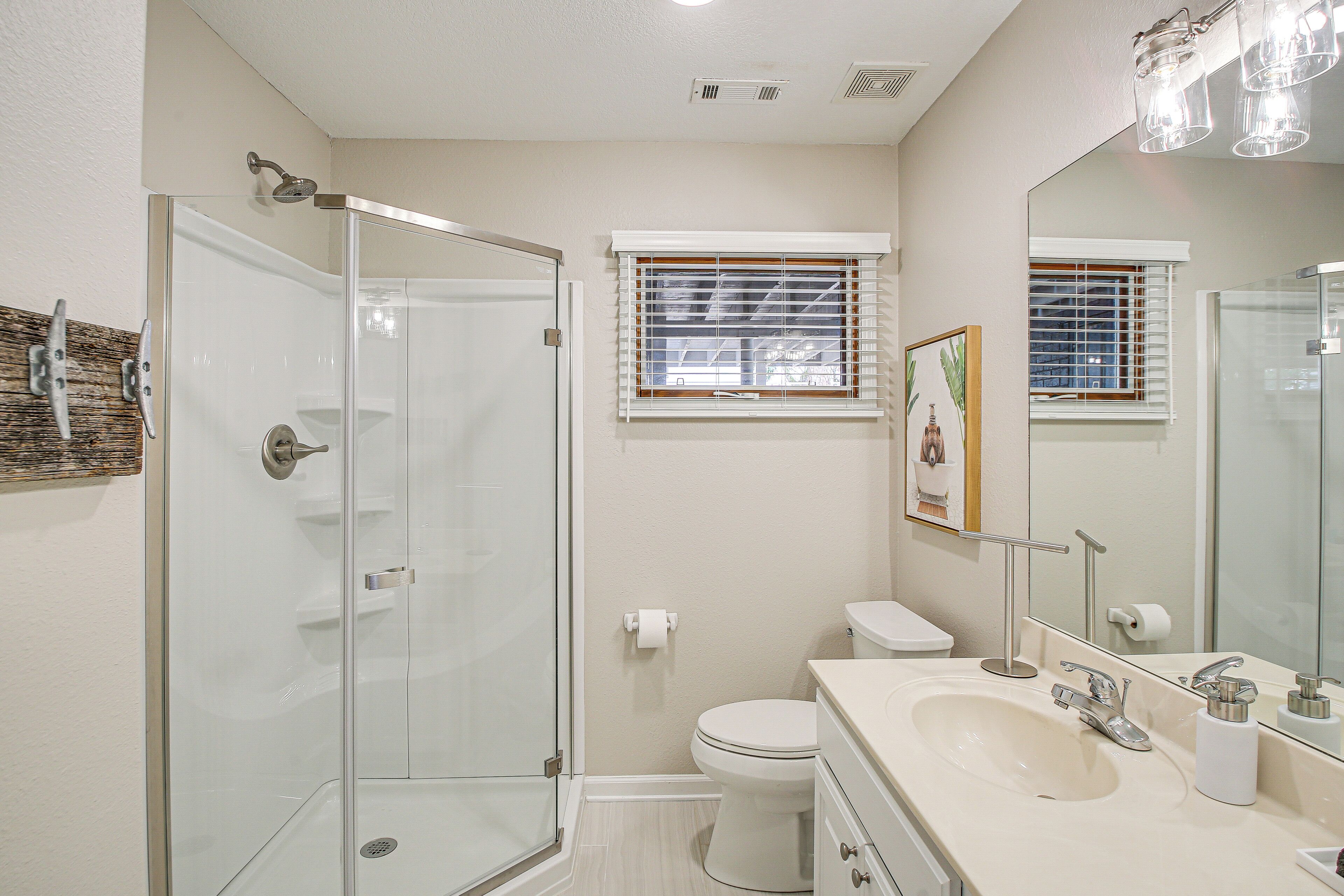 A bathroom with a glass-enclosed shower, a toilet, and a sink with a mirror.