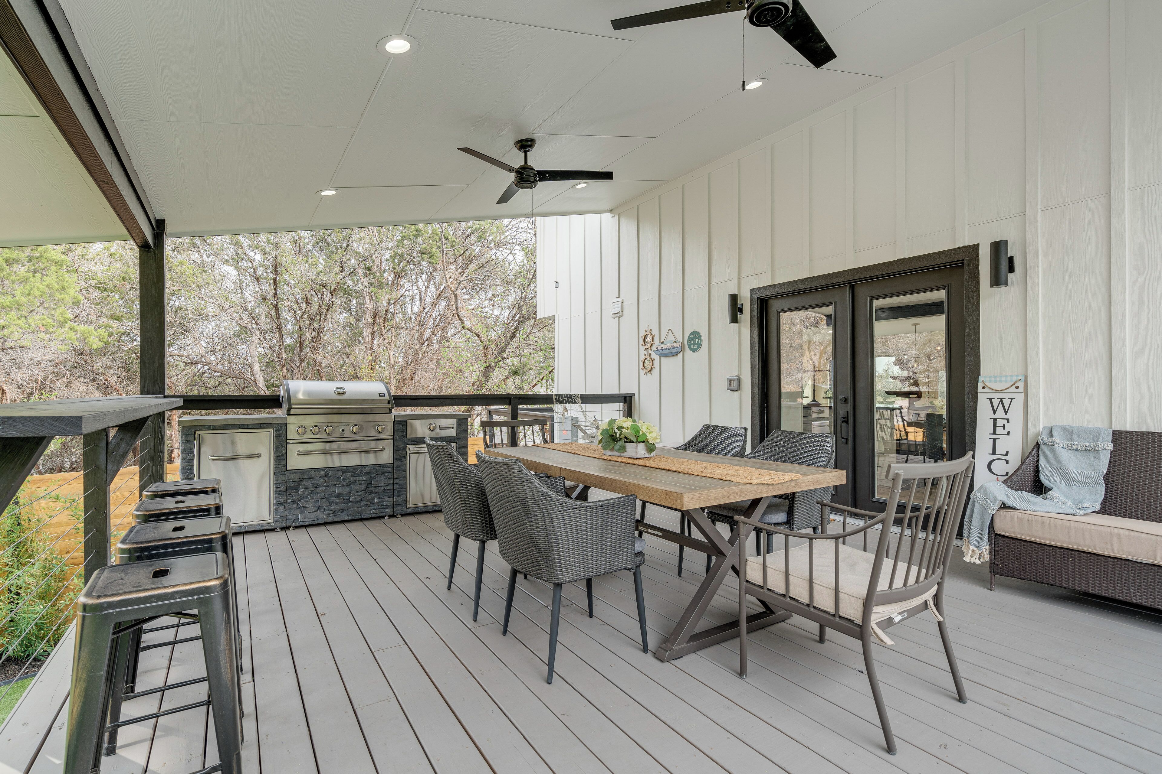 A covered outdoor patio with a wooden table, chairs, a grill, and a sofa.