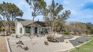Una casa moderna con techo inclinado, un porche delantero y un jardín ajardinado con caminos de grava y árboles.