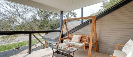 A covered porch with a swing chair, a table, and a view of the street.