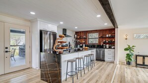 Una cocina moderna con una isla central, taburetes de bar, armarios de madera y vistas a una terraza exterior.