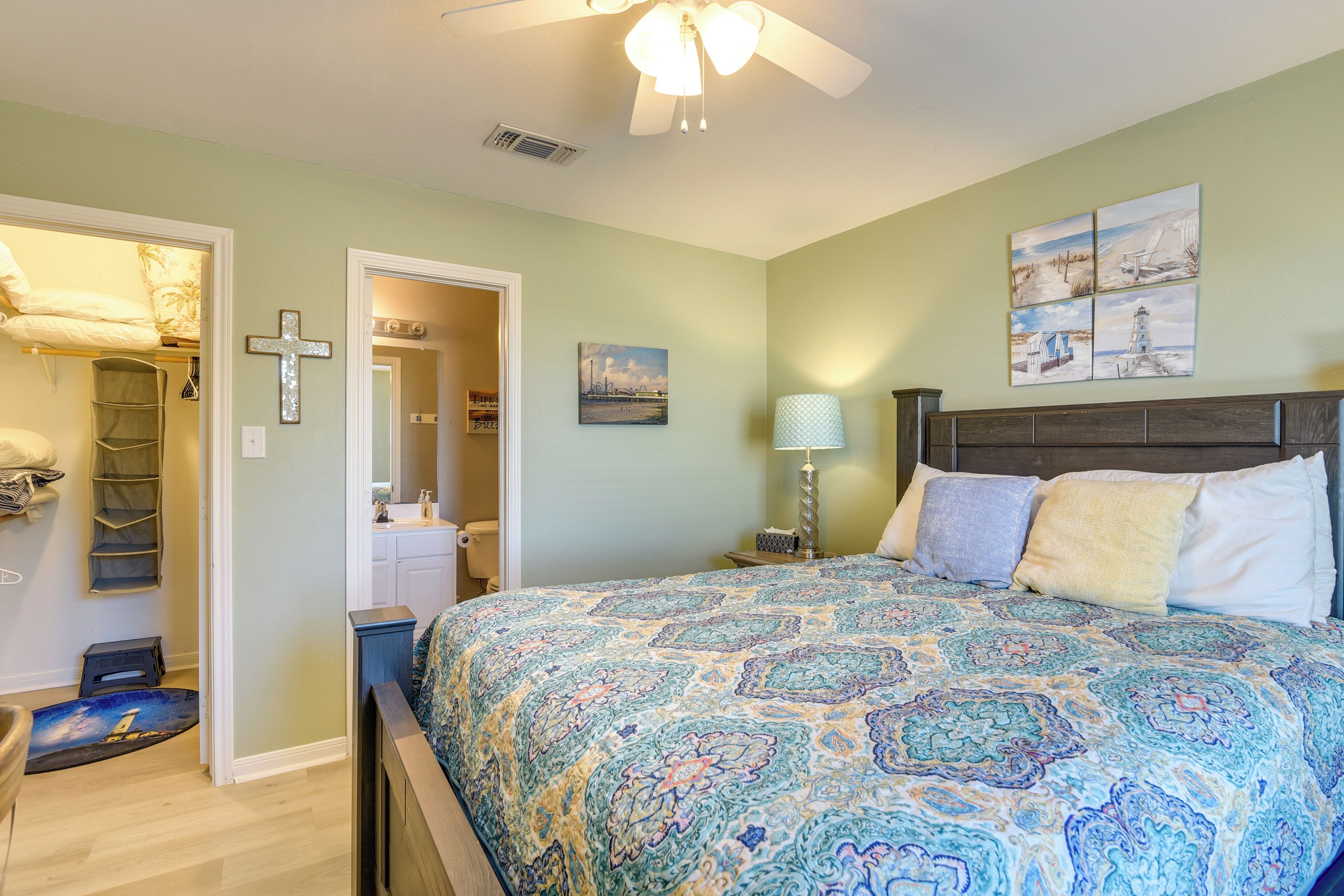 A bedroom with a patterned bedspread, a cross on the wall, and a painting above the bed.