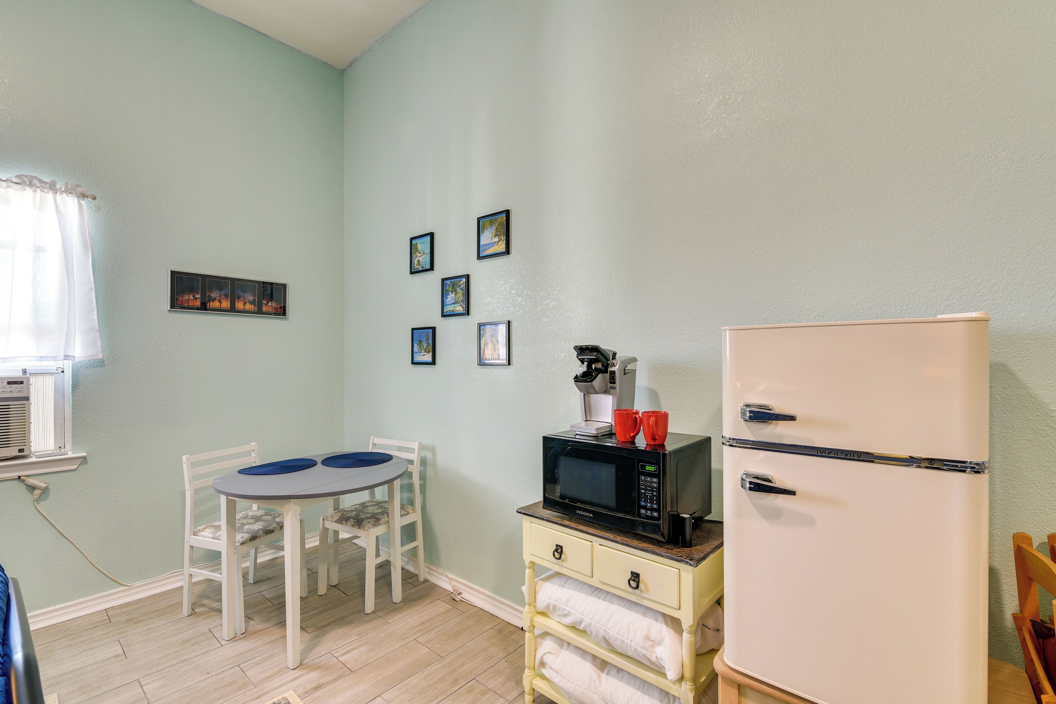 Una cocina compacta con un refrigerador blanco, un microondas y una pequeña mesa de comedor con sillas.