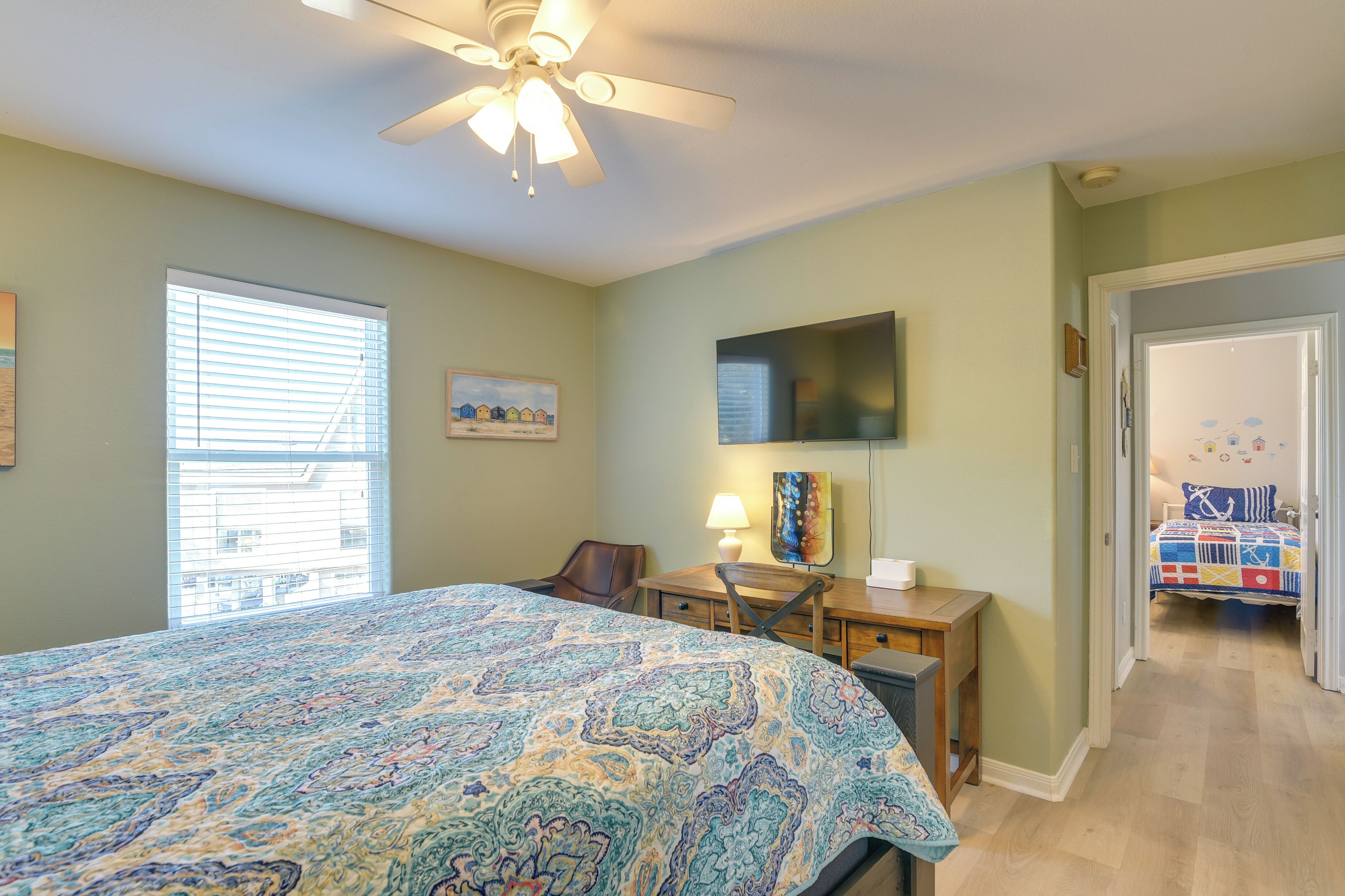 A bedroom with a bed, a desk, a chair, a TV, and a window.