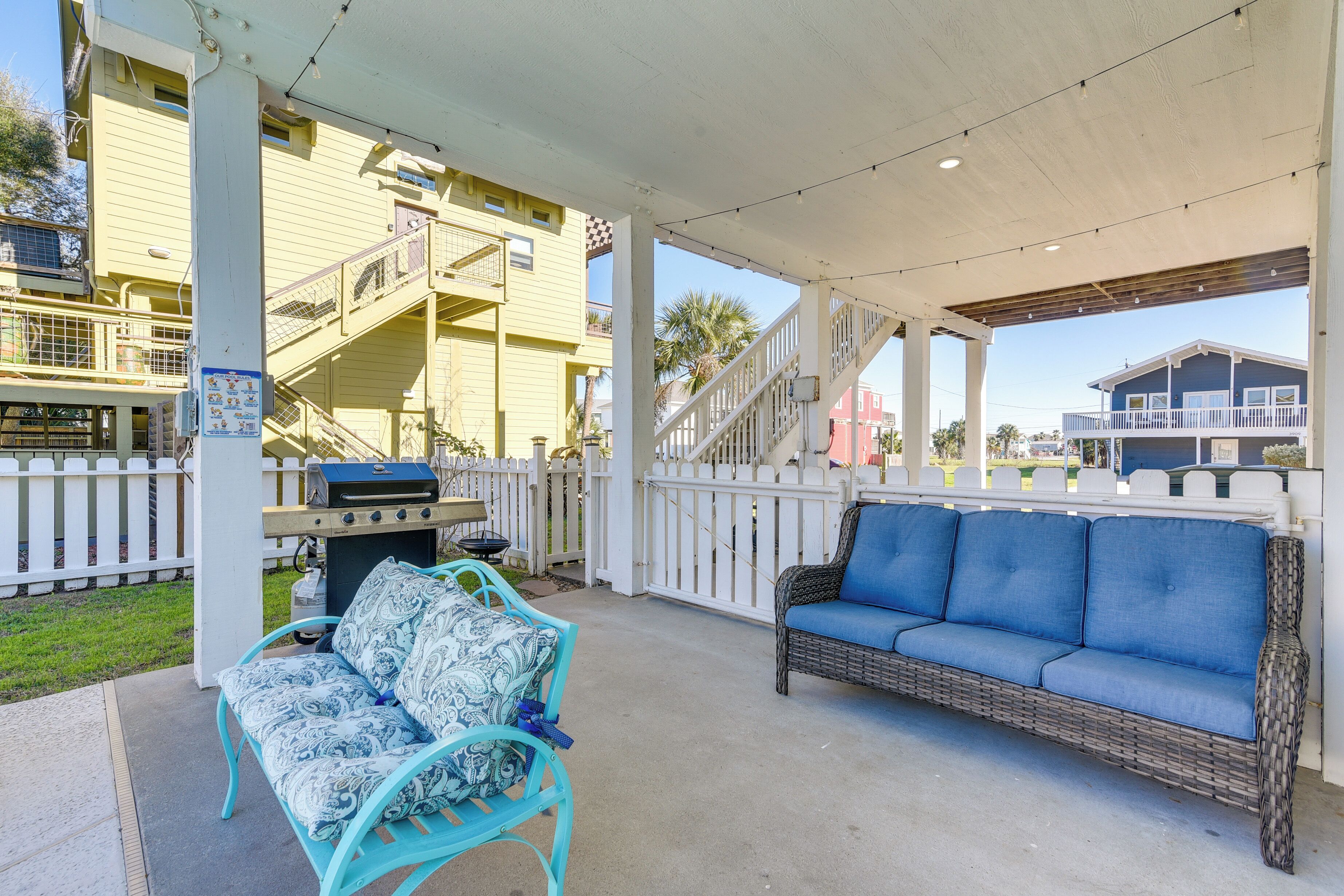 Eine überdachte Terrasse im Freien mit Grill, einem blauen Sofa und einem gemusterten Sessel.