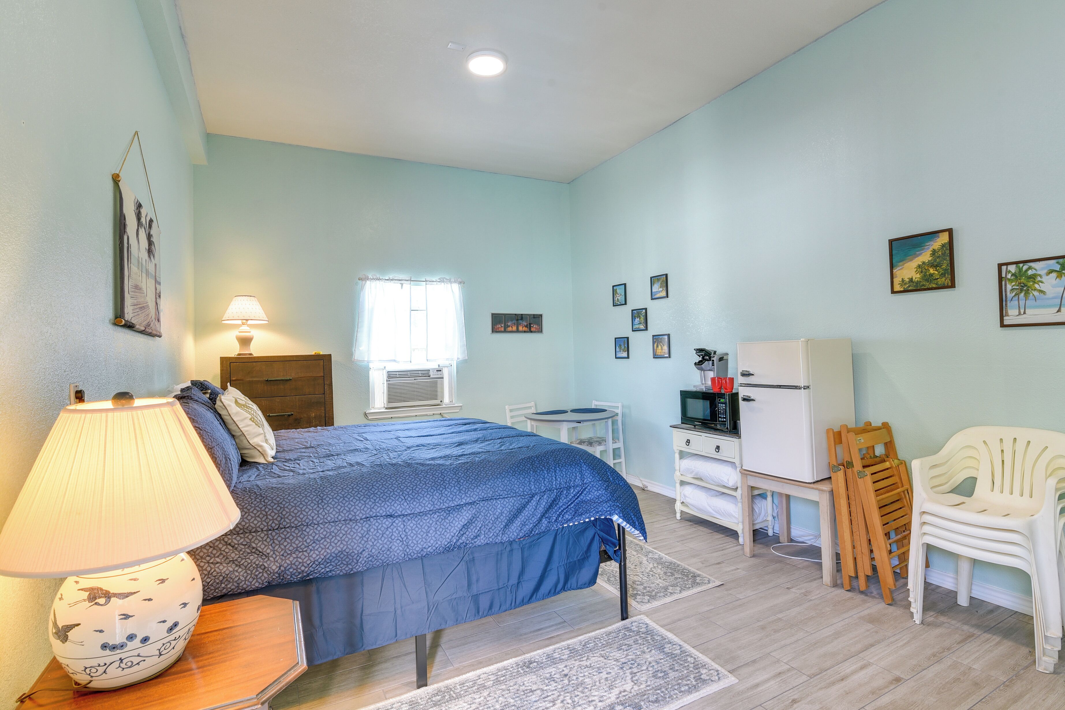 Een slaapkamer met een bed, een bedlampje, een dressoir, een televisie en een stoel.