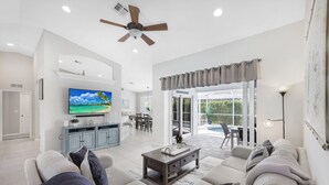 Ein geräumiges Wohnzimmer mit großem Fernseher, Deckenventilator und Blick auf die Terrasse.