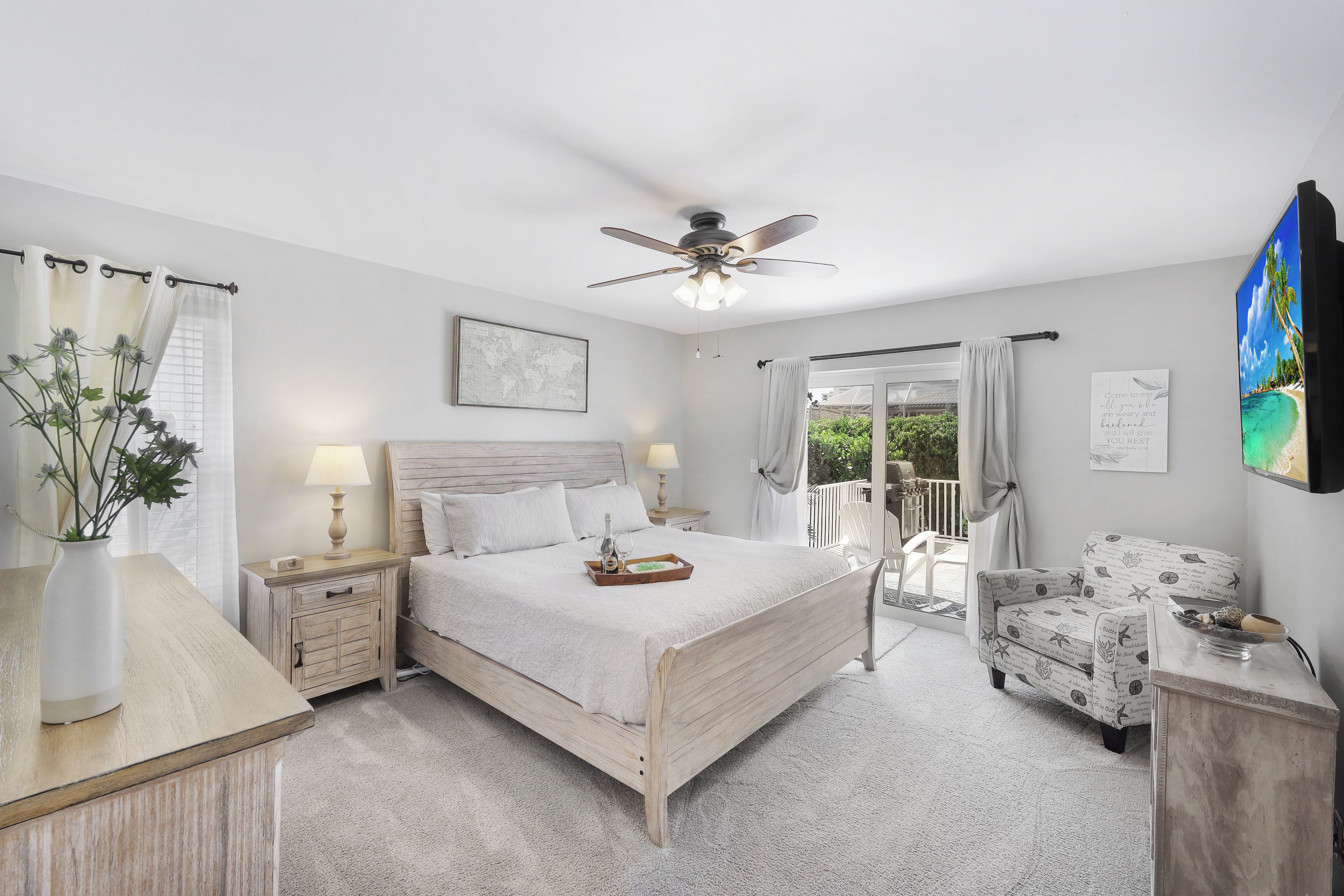 A bedroom with a bed, bedside tables, a ceiling fan, and a view of the outdoors.