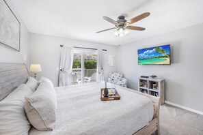 A bedroom with a bed, a ceiling fan, a TV, a bookshelf, and a view of the outdoors.