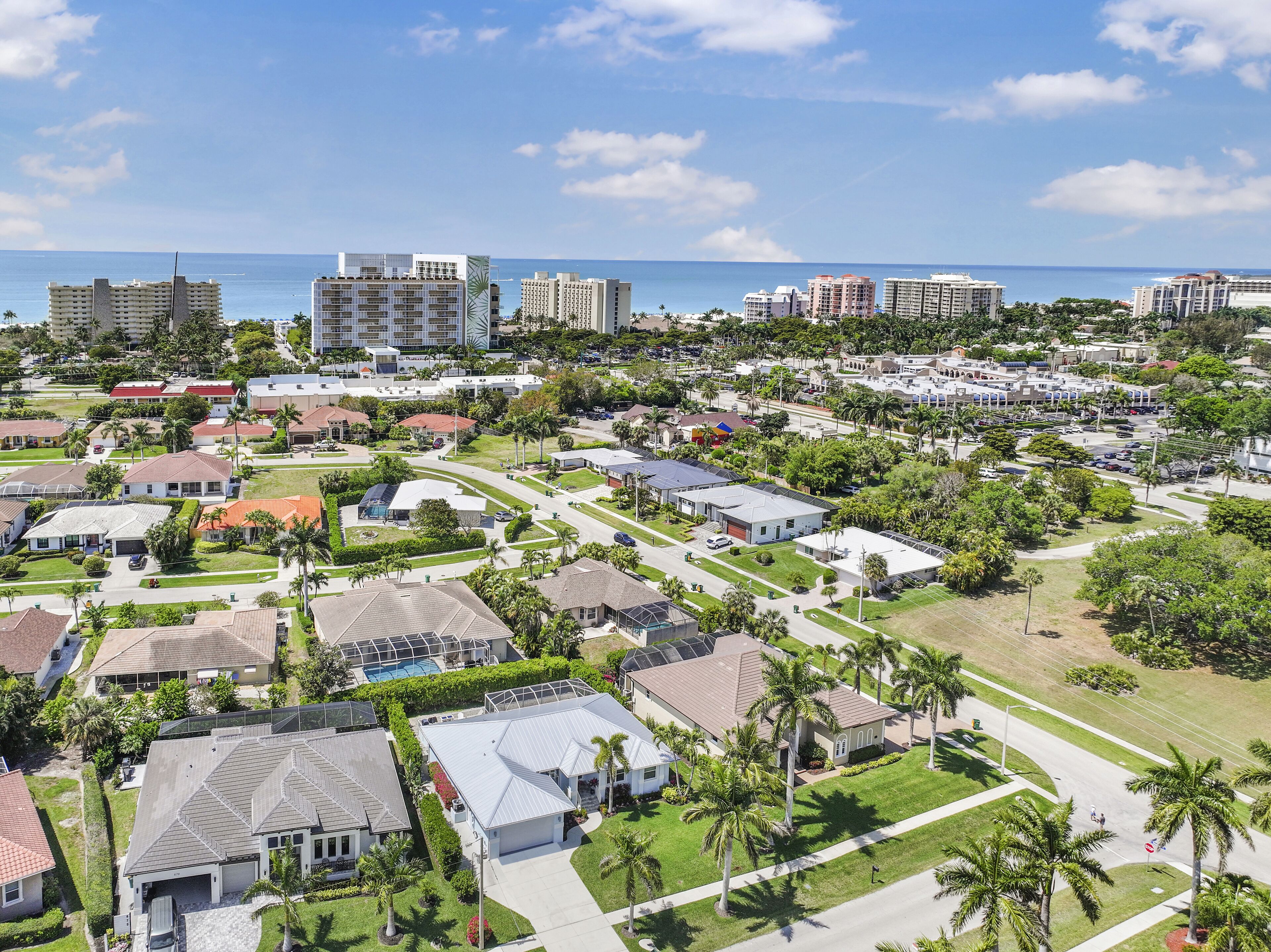 An aerial view of a residential area with houses, streets, and a beach in the background.