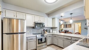 A modern kitchen with stainless steel appliances, a tiled backsplash, and light-colored cabinetry. - Lakefront Condo w/ Resort Amenities in Osage Beach (Osage Beach)