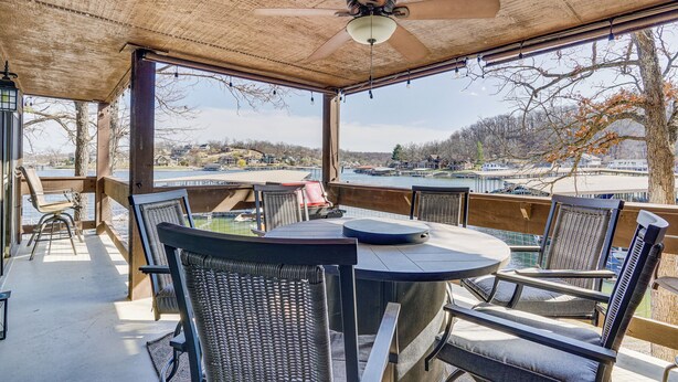 A covered outdoor seating area with a table and chairs, overlooking a body of water and a distant landscape. - Lakefront Condo w/ Resort Amenities in Osage Beach (Osage Beach)
