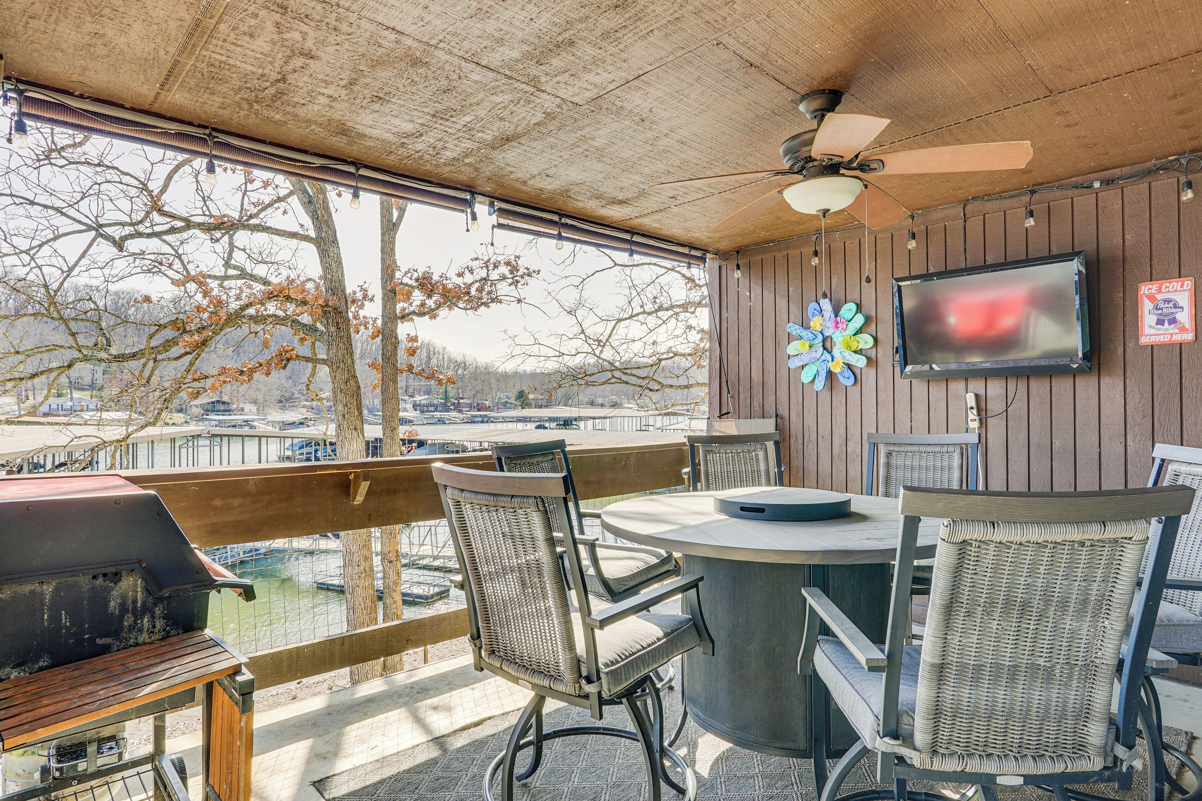 Une terrasse extérieure avec une table ronde, des chaises en osier, un barbecue et un téléviseur fixé au mur.