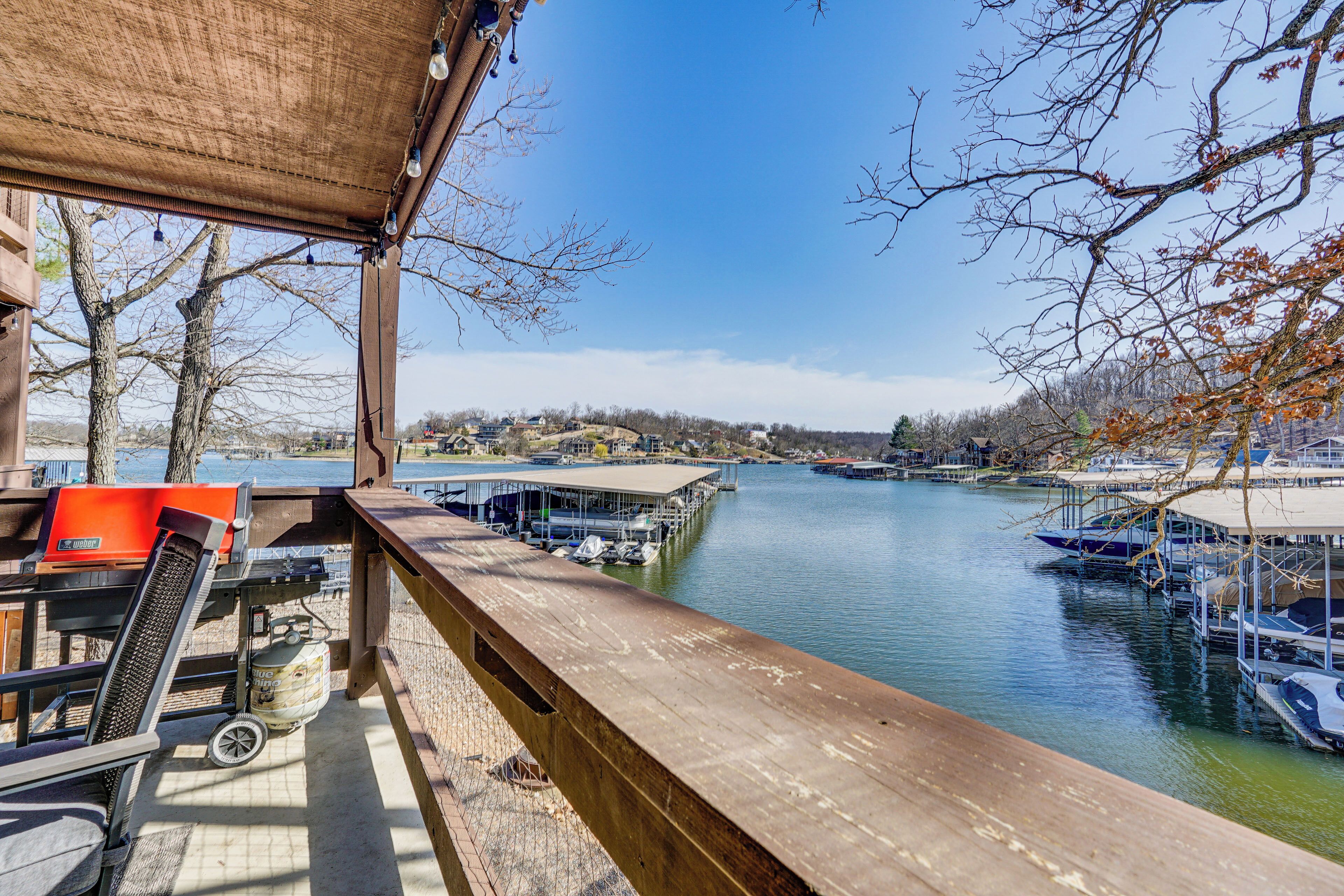 A wooden deck overlooking a marina with boats docked, a covered seating area, and a view of the water and distant buildings.