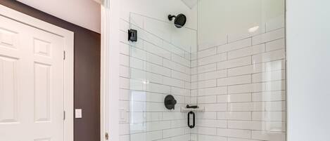 A modern shower with a glass door, white tiled walls, and a patterned floor.