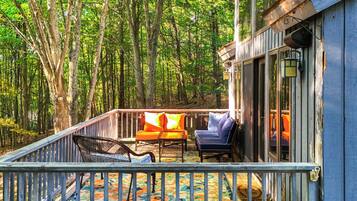 Relax on the deck surrounded by a serene forest, with a wicker chair and sofa for comfortable seating.
